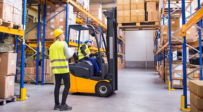 A worker operating a forklift while a co-worker looks on.