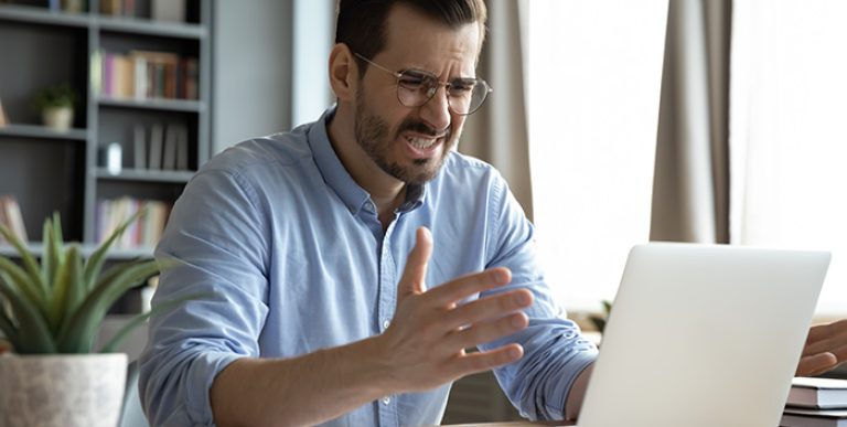 A person looking at a laptop in a frustrated manner.