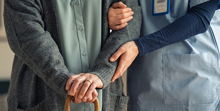 Close up hands of caregiver doctor helping old woman at clinic.