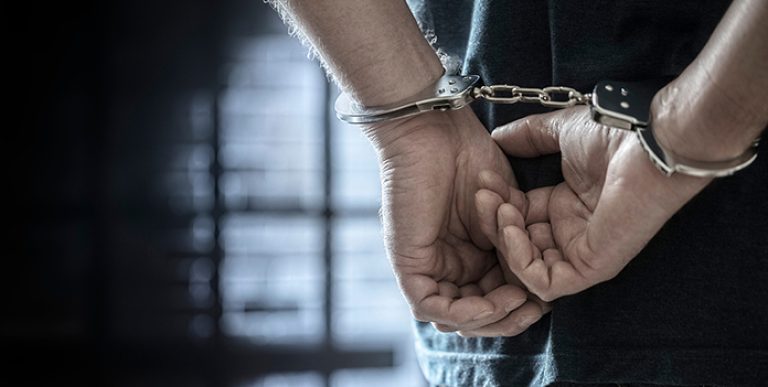 Arrested man in handcuffs with handcuffed hands behind back in prison