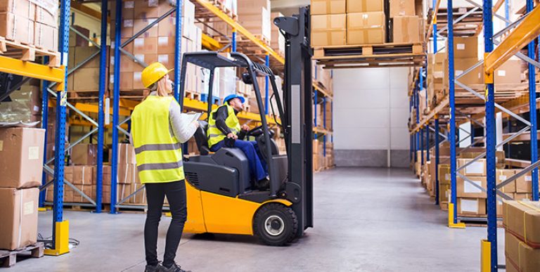A worker operating a forklift while a co-worker looks on.